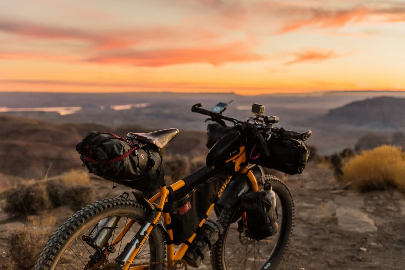 A loaded bikepacking setup with frame, seat and handlebar bags parked on a desert overlook at sunset
