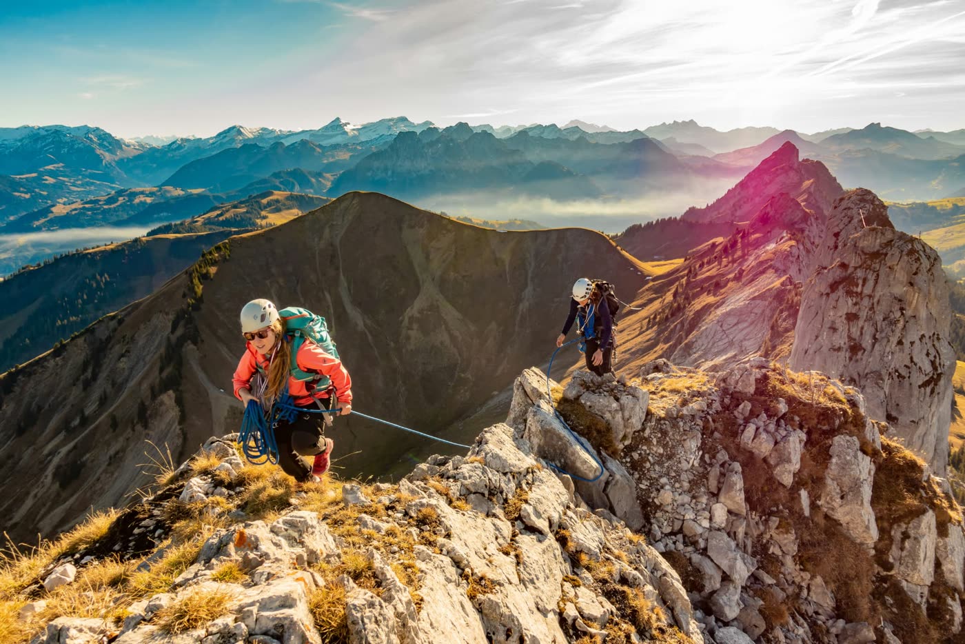 Two climbers in helmets and harnesses moving along a rocky mountain ridge with a rope between them