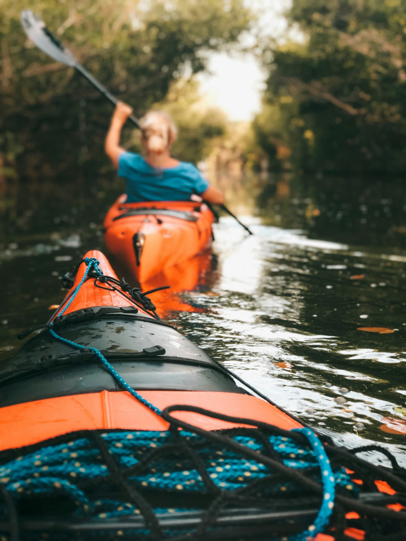 View from the back of a kayak following another paddler along a tree-lined river