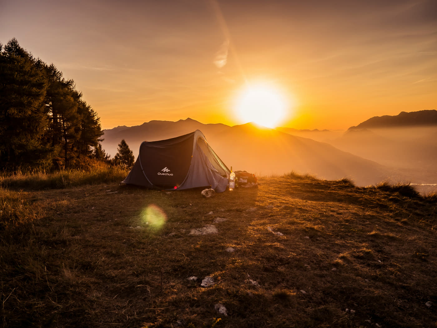 A small tent pitched on a grassy ridge at sunrise with mountains in the distance